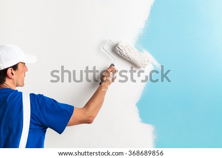 Back view of painter painting a wall with paint roller, with copy space