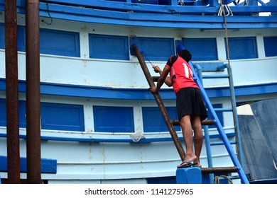 The back view of the painter is working on a painted wooden with a roller on a wooden boat. with a copy space.