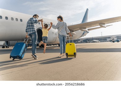 Back view of parents holding the hands of the child and going with suitcases to board the plane