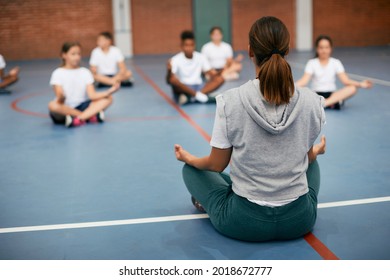 Back view of PE teacher leading Yoga class and meditating with elementary students at school gym. - Powered by Shutterstock