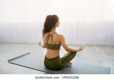 Back View Of Peaceful Indian Woman Sitting In Lotus Pose, Meditating, Reaching Inner Peace And Harmony On Mat At Home. Calm Young Lady Doing Breathing Exercises, Practicing Yoga In Morning