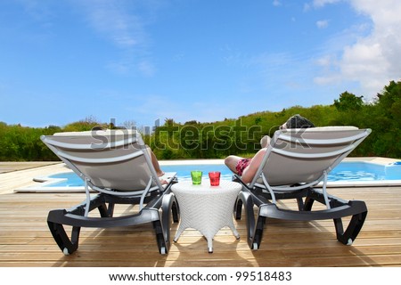 Back view of people relaxing on pool deck chairs