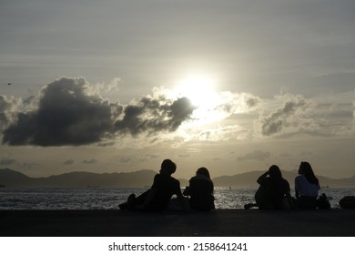 A Back View Of People Sitting Near The Sea During Sunset In Hong Kong, China