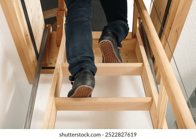 Back view of person using loft ladder or attic ladder. Woman climbing or going up loft sliding ladder to access attic space or loft. Space saving storage space. Selective focus. Lucerne, Switzerland.