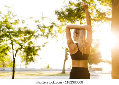 Back view photo of beautiful young blonde sports woman in park outdoors make stretching exercises. Stock Photo
