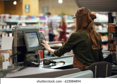 Back view photo of cashier woman on workspace in supermarket shop. Looking aside. - Shutterstock ID 623084894