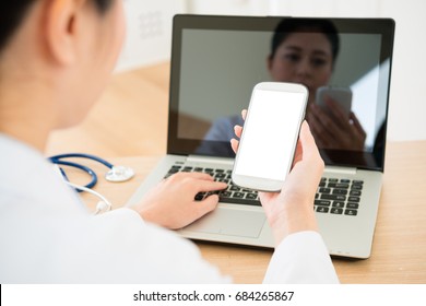 Back View Photo Of Pretty Young Doctor Looking At Mobile Cell Phone With Blank Screen When She Using Laptop Working In Office Through Online Service System. Selective Focus Photo.