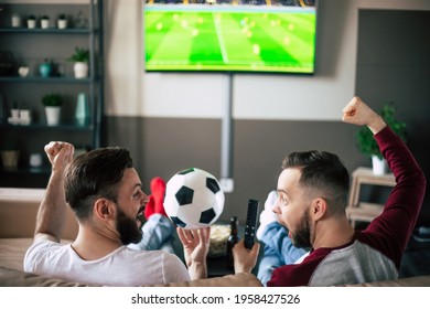 Back view photo of two best friends and fans of football watching some sport match on the TV and drinking beers and eating snacks while cheering for the team on the couch