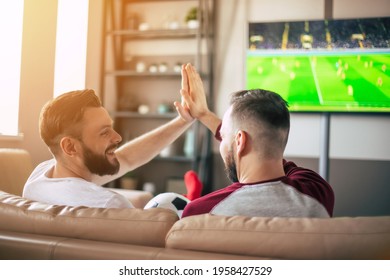 Back View Photo Of Two Best Friends And Fans Of Football Watching Some Sport Match On The TV And Drinking Beers And Eating Snacks While Cheering For The Team On The Couch