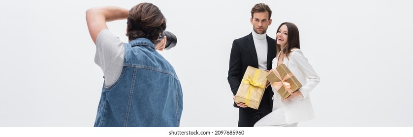 Back View Of Photographer Taking Photo Of Stylish Models With Gift Boxes Isolated On White, Banner