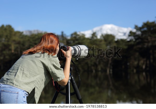 Back view of a photographer taking\
pphotos with tele lens and dslr camera in the\
mountain