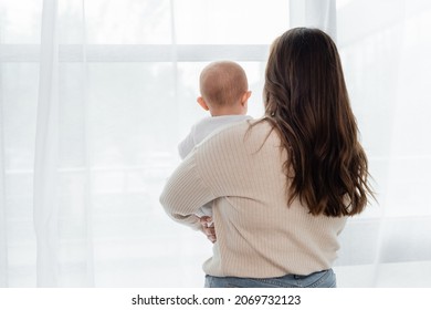 Back view of plus size woman holding baby near window at home - Powered by Shutterstock