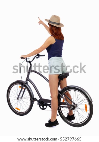 back view of pointing woman with a bicycle. cyclist sits on the bike. Rear view people collection.  backside view of person. Girl in a straw hat shows his hand forward while sitting on the bike.
