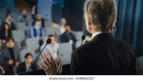 Back view of politician or activist pronouncing speech during press campaign in the conference hall. Mature organization representative answers questions, gives interview to journalists for media.