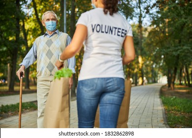 Back View Portrait Of Adult Woman Bringing Shopping Bags With Foodstuff For Old Caucasian Man