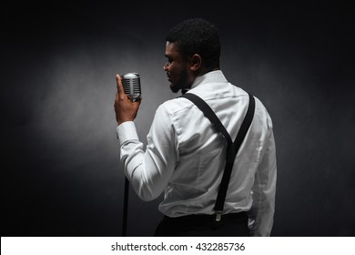 Back view portrait of afro american man singing into vintage microphone over dark background