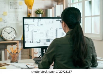 Back view portrait asian woman engineer working desktop computer and blueprints screen in office  young female architect worker sitting in studio looking at pc screen interior design plan