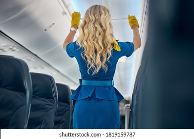 Back View Portrait Of Beautiful Female Air Hostess In Blue Uniform Showing Airplane Rules For Safety On Board