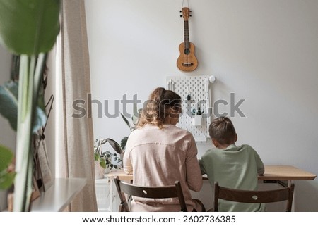 Back view portrait of caring single mother helping son doing homework in cozy home interior, copy space