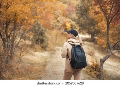 Back View Portrait Of Caucasian Plus Size Woman 30-35 Years Old With Backpack In Beige Sportswear Walking In The Fall Woods On Vacations. Healthy And Wellness Lifestyle Concept. People From Behind.