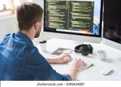 Back view portrait of contemporary web developer writing code for program sitting at desk and working on startup project in modern office, copy space