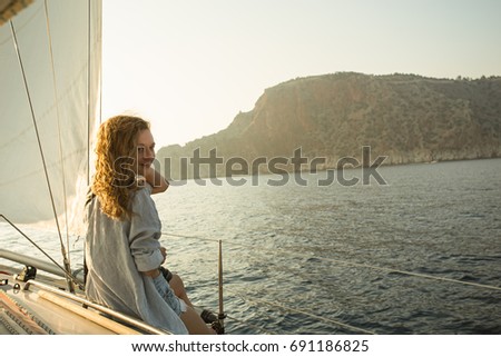 Back view portrait of fit blonde woman with wavy hair sitting at yacht deck and watching sea and mountains