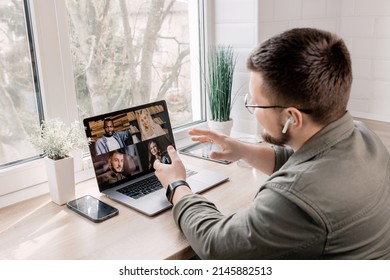 Back View Portrait Of Happy Businessman Explaining The Moments Of A New Project To Colleagues On Video Meeting,sitting At The Desk In Home Office.Stylish Male Freelancer Is Having An Online Conference