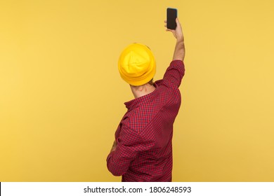 Back view portrait of hipster guy in beanie hat and checkered shirt talking video call, taking selfie on mobile phone, holding smartphone up with mock up blank display. indoor studio shot isolated - Powered by Shutterstock