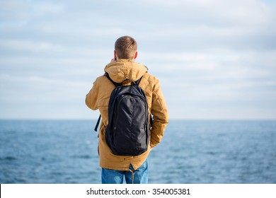 Back view portrait of a man with backpack talking on the phone with sea on background