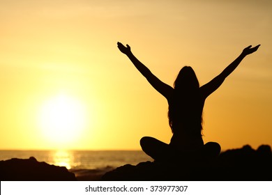 Back view portrait silhouette of a happy woman raising arms in a new day looking at warm sun at sunrise on the beach with the sea in a beautiful background - Powered by Shutterstock