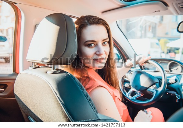 Back view Portrait of smiling business lady,\
caucasian young woman driver looking at camera and smiling over her\
shoulder while driving a car. Selective focus, copy space. Inside\
view
