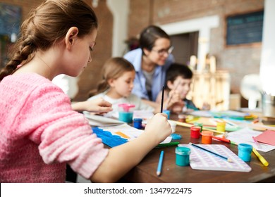 Back view portrait of teenage girl painting picture in art class with group of children, copy space