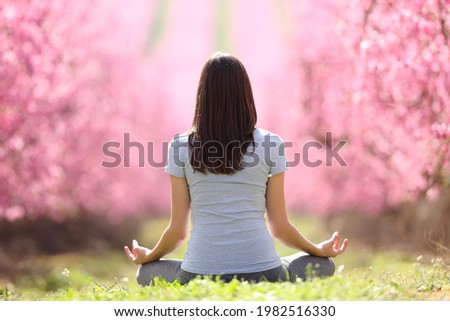 Back view portrait of a woman doing yoga exercise in a pink flowered field