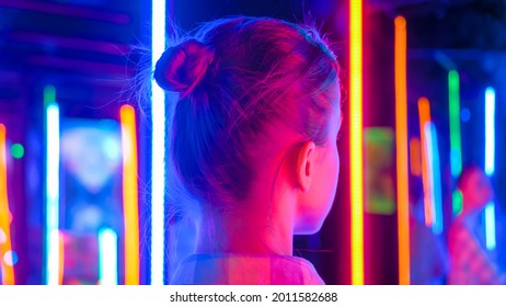 Back view - portrait of woman looking right at interactive exhibition or museum with colorful fluorescent tube illumination. Futuristic, retrowave, immersive, entertainment concept - Shutterstock ID 2011582688
