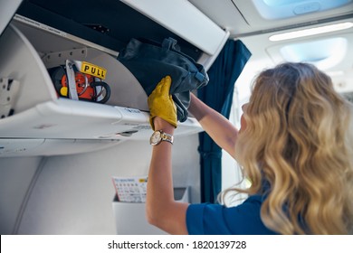 Back View Portrait Of Young Air Hostess Putting Luggage In The Cabin Compartment