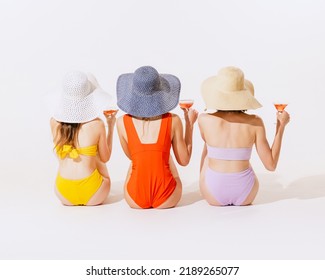 Back view portrait of young women sitting in swimming suit sitting, drinking cocktails isolated over grey background. Concept of beauty, fashion, retro style, summertime, party. Copy space for ad