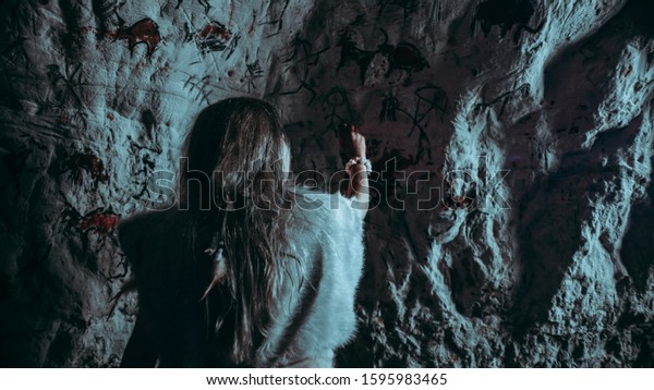 Back View of Primitive Prehistoric Neanderthal\
Child in Animal Skin Draws Animals and Abstracts on Walls. Creating\
First Cave Art with Petroglyphs, Rock Paintings. Shot Made at Night\
with Cold Light