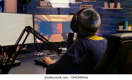 Back View Of Pro Streamer Playing Video Game Competition Use Professional Setup With Streaming Chat Open. Gamer Sitting On Gaming Chair Using Professional Headphones Late At Night In Home Studio