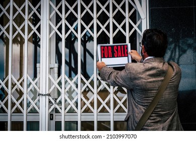 Back view of professional business man putting for sale box panel on the closed door of a store  concept of selling and buying properties and economy crisis - seller or owner close his activity 