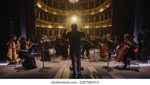 Back View of Professional Conductor Directing Symphony Orchestra with Performers Wearing Medical Masks, Playing Violins, Cello and Trumpet on Classic Theatre with Curtain Stage During Music Concert - Shutterstock ID 2287585913