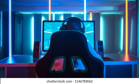 Back View of Professional Gamer Playing in First-Person Shooter Online Video Game on His Personal Computer. Room Lit by Neon Lights in Retro Arcade Style. Cyber Sport Championship.