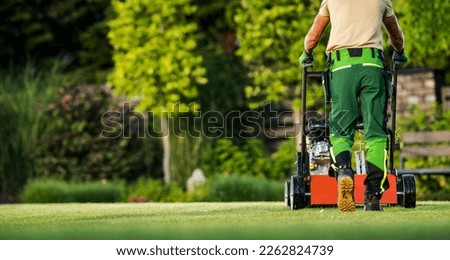 Back View of Professional Gardener Mowing the Backyard Lawn with Push Mower. Garden Care and Maintenance Theme.