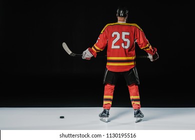 Back View Of Professional Ice Hockey Player Holding Hockey Stick On Black 