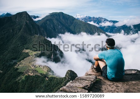 Back view of professional man dressed in active wear resting on peak of mountain and admiring green hills of Machu Picchu and breathtaking scenery of natural environment during trekking wanderlust