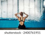 Back view of a professional swimmer sitting near pool and adjusting her swimming goggles before training.