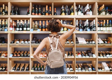 Back view puzzled minded young woman in casual clothes shopping at supermaket grocery store buy choosing wine alcohol bottle scratch head inside hypermarket. People purchasing gastronomy food concept - Powered by Shutterstock