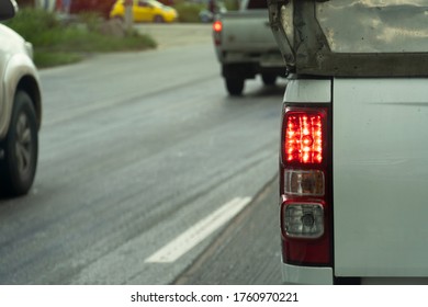 Back View Of Rear Side White Pick Up Car Drive On The Road. With Open Brake Light.