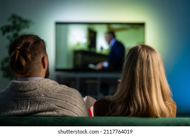 Back View Of Relaxed Caucasian Couple Sitting Together On Couch And Watching Movie On TV. Happy Family Spending Evening Time At Home With Fascinating Film.