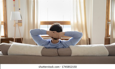 Back View Of Relaxed Caucasian Man Sit Rest On Comfortable Couch Hands Over Head Look In Window Distance Dreaming, Calm Male Relax On Sofa In Living Room, Enjoy Home Weekend, Stress Free Concept