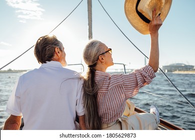 Back View Of Relaxed Mature Couple Sitting On Yacht. Stylish Woman Waving Hat During Boat Trip.